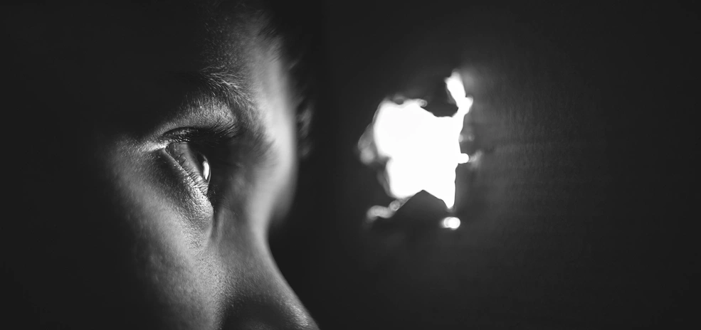 A kid's eyes looking through a hole in a cardboard box.