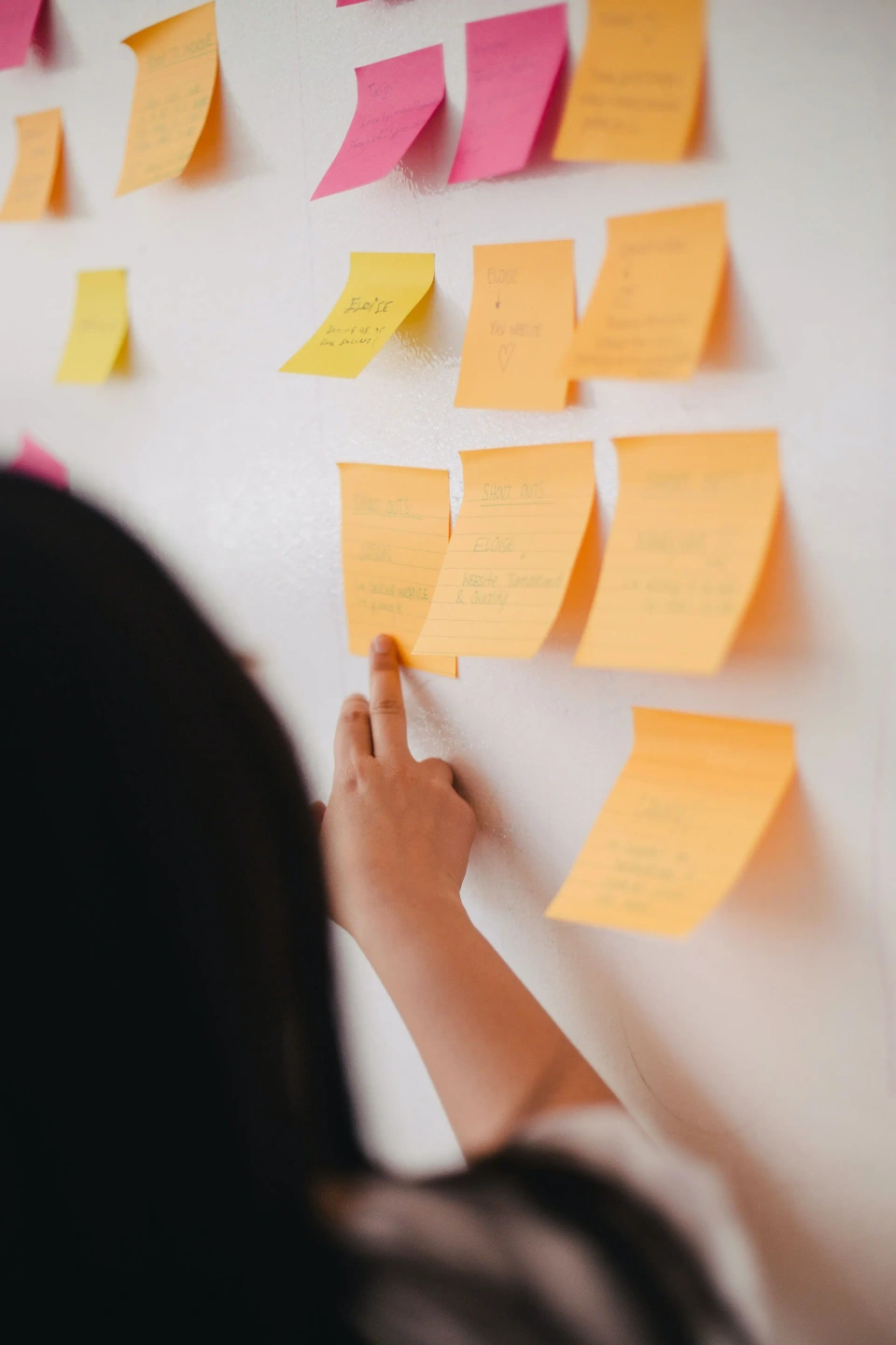 A hand pointing to a sticky note on a wall